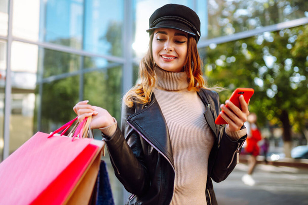 Young woman after shopping with phone. Autumn style. Online shopping concept.  Purchases, black friday, discounts, sale concept.  - Photo, Image