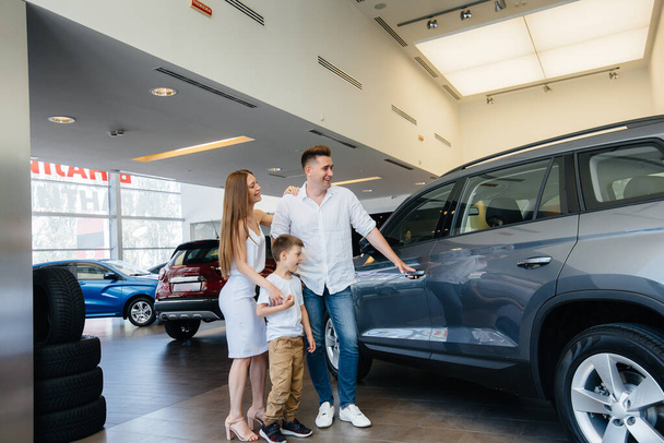 A happy young family chooses and buys a new car at a car dealership. Buying a new car - Фото, изображение