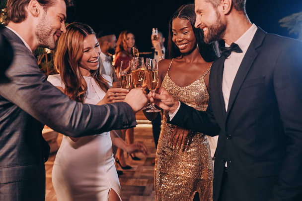 Grupo de personas en ropa formal brindando con champán y sonriendo mientras pasan tiempo en una fiesta de lujo - Foto, Imagen