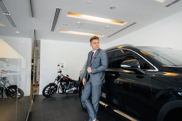 A young businessman looks at a new car in a car dealership. Buying a car - Foto, imagen