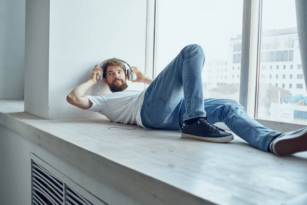 cute man lying near the window wearing headphones fun - Photo, image