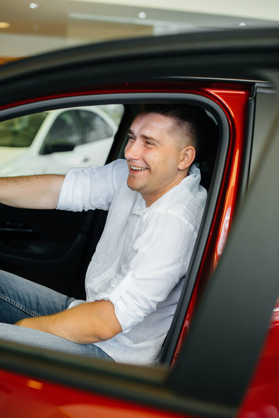 A young man is sitting in the cabin of a new car and testing it. Buying a car - Photo, Image