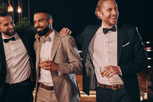 Three handsome men in suits bonding and drinking whiskey while spending time on party - Foto, Bild