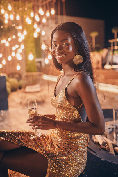 Kaunis nuori afrikkalainen nainen iltapuvussa pitäen huilua samppanjalla ja hymyillen - Valokuva, kuva