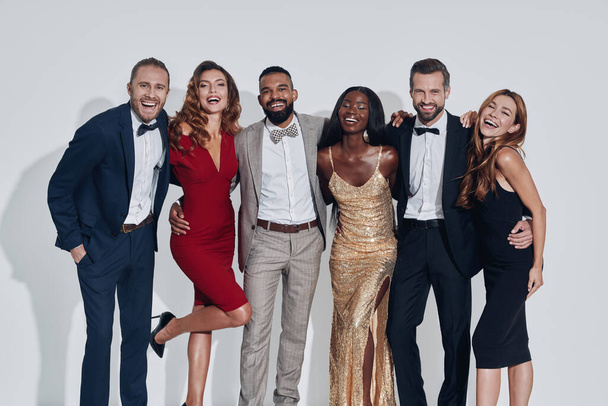 Group of beautiful people in formalwear bonding and smiling while standing against gray background - Photo, image
