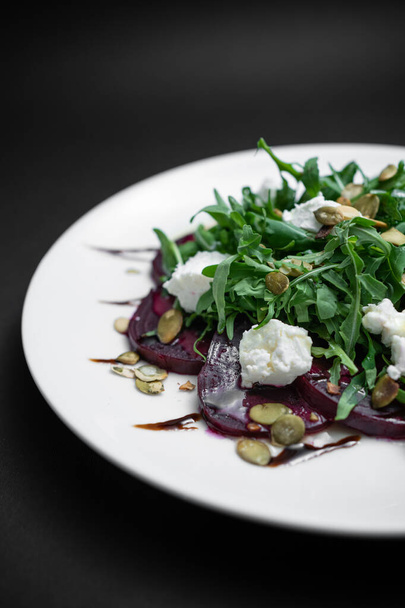 salad with beet, arugula and feta cheese on white plate on black background - Zdjęcie, obraz