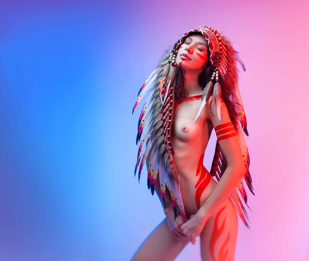 femme nue en costume amérindien avec des plumes sur un fond néon - Photo, image
