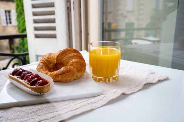 Γαλλικό πρωινό, φρέσκο ψημένο κρουασάν βουτυράτο ζαχαροπλαστικής σερβίρεται με νόστιμο χυμό πορτοκαλιού και παλιά γαλλικά σπίτια στο παρασκήνιο - Φωτογραφία, εικόνα