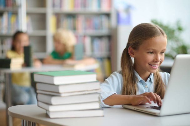 Pleased beautiful schoolchild typing on the laptop - Photo, Image