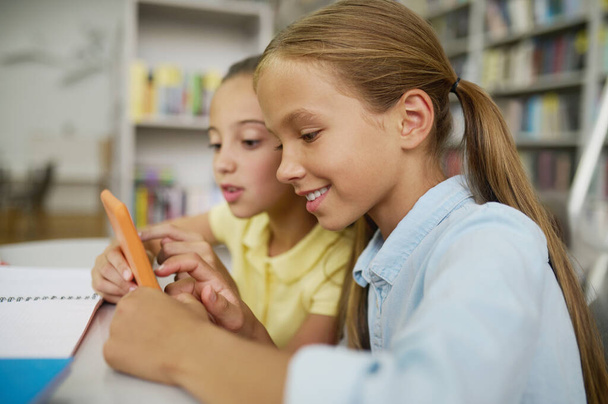 Two classmates using a gadget at a public library - Фото, изображение