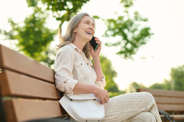 Joyful woman with handbag talking on smartphone - Foto, imagen