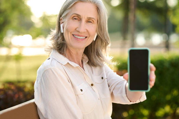 Good looking retirement age woman showing smartphone - Foto, Bild