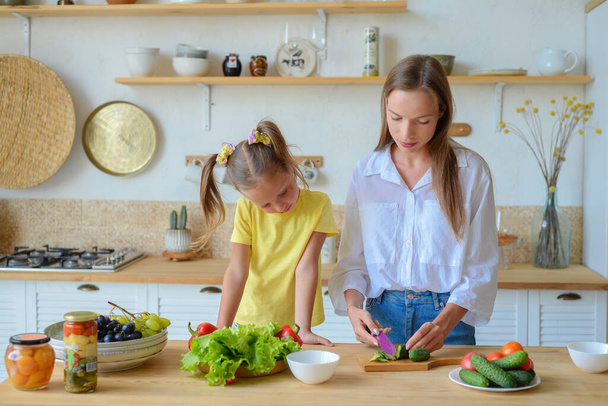 moeder leert weinig dochter naar koken gezond voedsel in de keuken - Foto, afbeelding