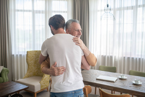 Gray-haired mature man hugging his sona and looking happy - Foto, imagen