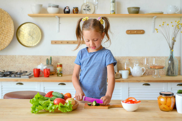 Маленькая девочка на кухне режет овощи для салата. концепция правильного питания и вегетарианства - Фото, изображение