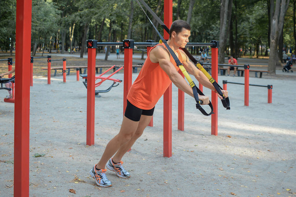 sports guy is exercising in the park on the playground in summer - Foto, Bild