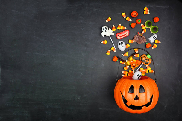 Halloween Jack o Lantaarn emmer met morsend snoep, bovenaanzicht op een zwarte achtergrond met kopieerruimte - Foto, afbeelding