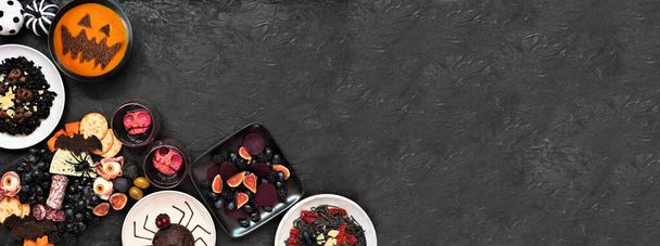 Die Eckecke der Halloween-Dinner-Party grenzt an einen dunkelschwarzen Banner-Hintergrund. Von oben gesehen. Wurstbrett, schwarzes Risotto und Nudeln, Spinnenkuchen, Laternen-Kürbissuppe und Apfelschädel-Wein. - Foto, Bild