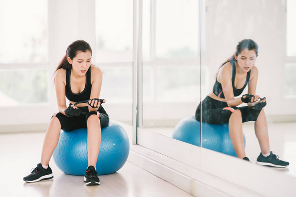 Young, determined Asian woman exercise alone at home gym or sports club, sit on fitness ball with mirror. Yoga aerobic class, sport trainer, weight loss, or healthy wellbeing lifestyle concept - Photo, Image