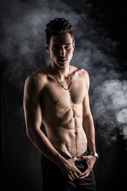 Lean athletic shirtless young man standing on dark background - Foto, imagen