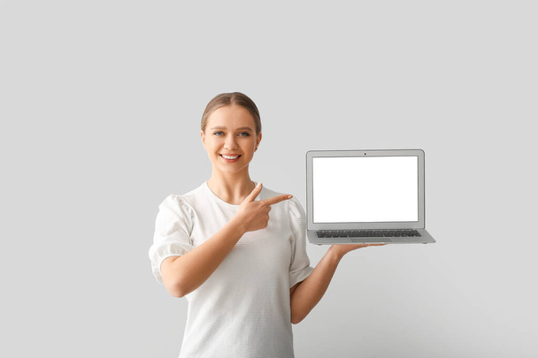 Gyönyörű fiatal nő gazdaság laptop üres képernyő szürke háttér - Fotó, kép