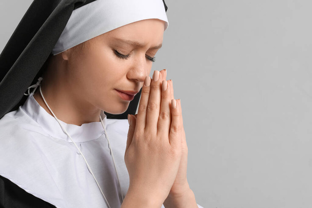 Młoda modląca się zakonnica na szarym tle - Zdjęcie, obraz