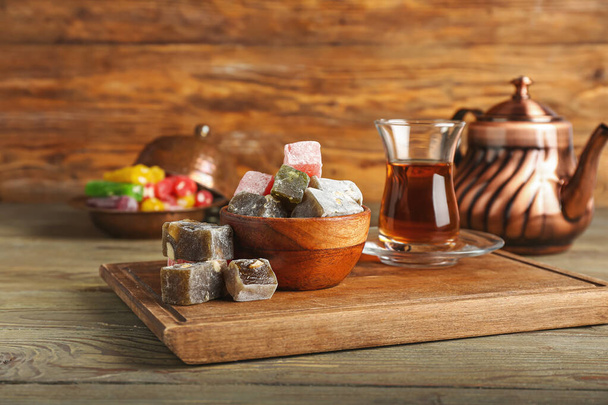 Schaal met lekker Turks genot en een glas thee op houten ondergrond - Foto, afbeelding