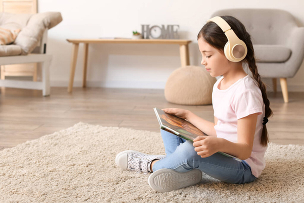 Kislány fejhallgatóval olvasókönyv otthon - Fotó, kép