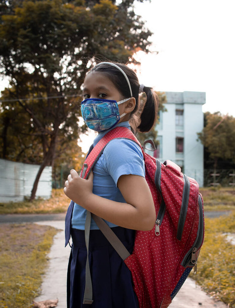 Portrét šťastné indické dívky dítě student v modré školní uniformě s červenou taškou a nosní maskou ochrana jít do školy - Fotografie, Obrázek