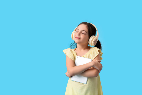 Little girl with tablet computer and headphones on color background - Fotografie, Obrázek