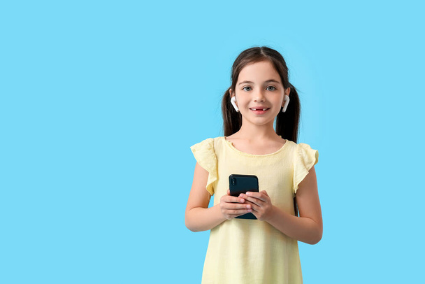Little girl with earphones and mobile phone on color background - Photo, Image