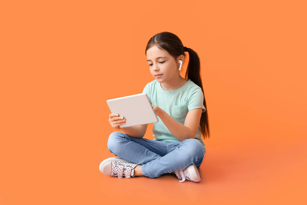 Little girl with tablet computer and earphones on color background - Photo, Image