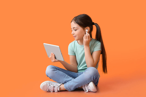 Маленькая девочка с планшетным компьютером и наушниками на цветном фоне - Фото, изображение