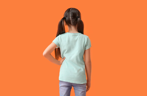 Маленькая девочка в стильной футболке на цветном фоне, вид сзади - Фото, изображение