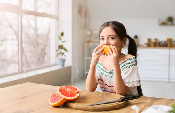 Κοριτσάκι τρώει φρέσκα γκρέιπφρουτ στην κουζίνα - Φωτογραφία, εικόνα
