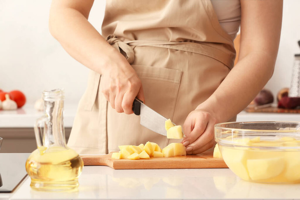 Young woman cutting potato for delicious borscht on wooden board in kitchen - Photo, Image
