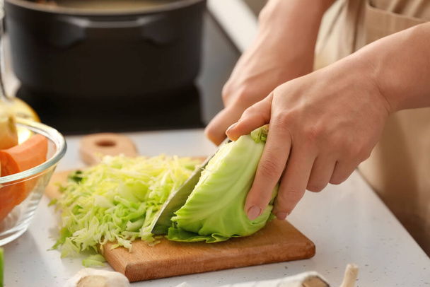 Young woman cutting cabbage for delicious borscht on wooden board in kitchen - Photo, Image
