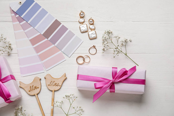 Свадебные кольца, стильные аксессуары, образцы цветов и подарочные коробки на белом деревянном фоне - Фото, изображение