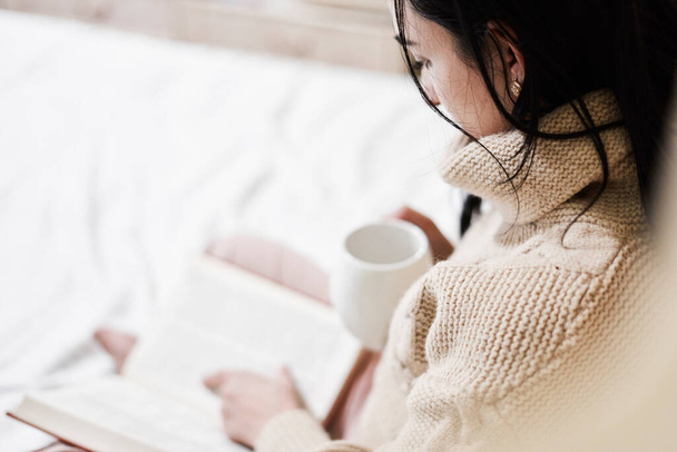 Mujer joven bebiendo café y leyendo un libro en la cama - Foto, Imagen