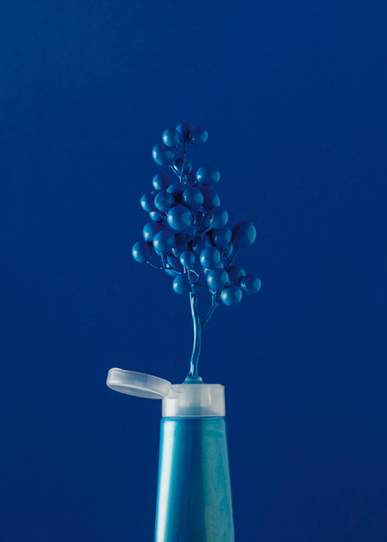 Blue grapes come out from blue tube of paint on blue background. Creative idea of summer or autumn fruit and nature concept. Colorful fruit inspiration. - Foto, imagen