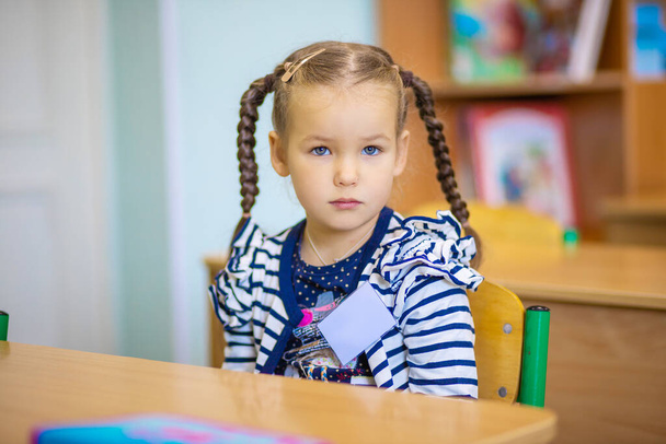 little pretty girl sits at a desk at school, a schoolgirl in a class, a child smiles, back to school, teaching in elementary grades, children in class, school weekdays. - Photo, Image