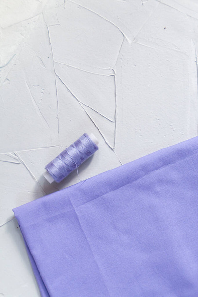 Иголка и хлопчатобумажная ткань фиолетового цвета на сером фоне, медленная мода и домашняя концепция шитья - Фото, изображение