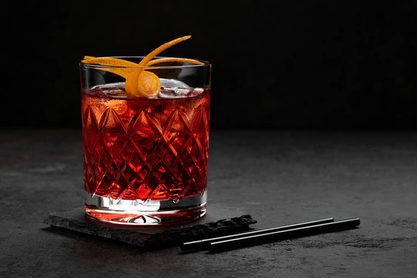 Classic Negroni Cóctel en un vaso retro con hielo y cáscara de naranja sobre fondo negro, espacio para el texto - Foto, Imagen