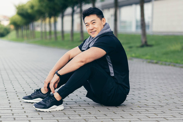 asian man after fitness workout and jogging sitting on the ground tired resting - Fotó, kép
