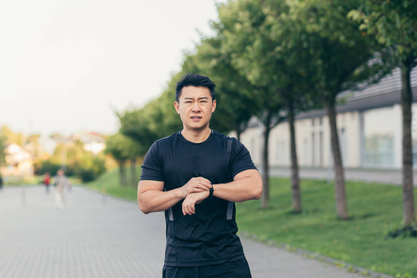 Male asian athlete, tired after a morning jog, runs in the park near the stadium - 写真・画像
