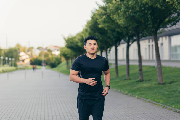 Male asian athlete running in the park in a backpack before work, running in the park near the stadium - 写真・画像