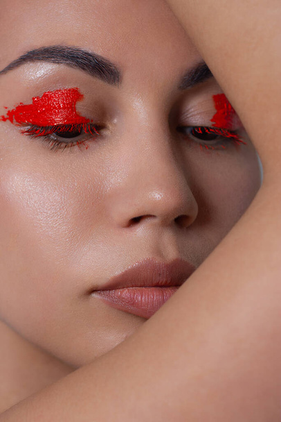 Close-up beauty of young brunette woman with fashion evening makeup with perfect skin. Black eyeliner on the eyes and extremely long eyelashes, neon red liner and nude lipstick on the lip - Fotoğraf, Görsel