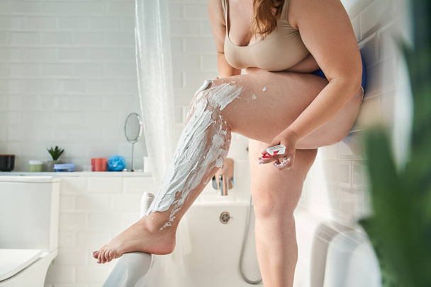Healthy plus size girl shaving her legs carefully - Foto, Imagen