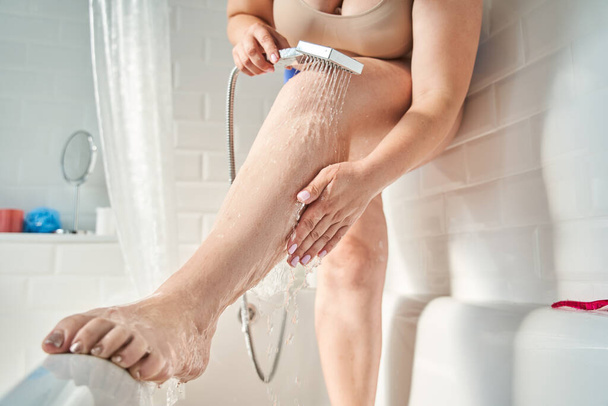 Woman washing leg in shower while standing in bath - Фото, зображення