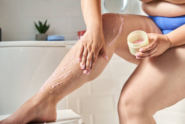 Woman massaging legs with body cream in bathroom - Фото, изображение
